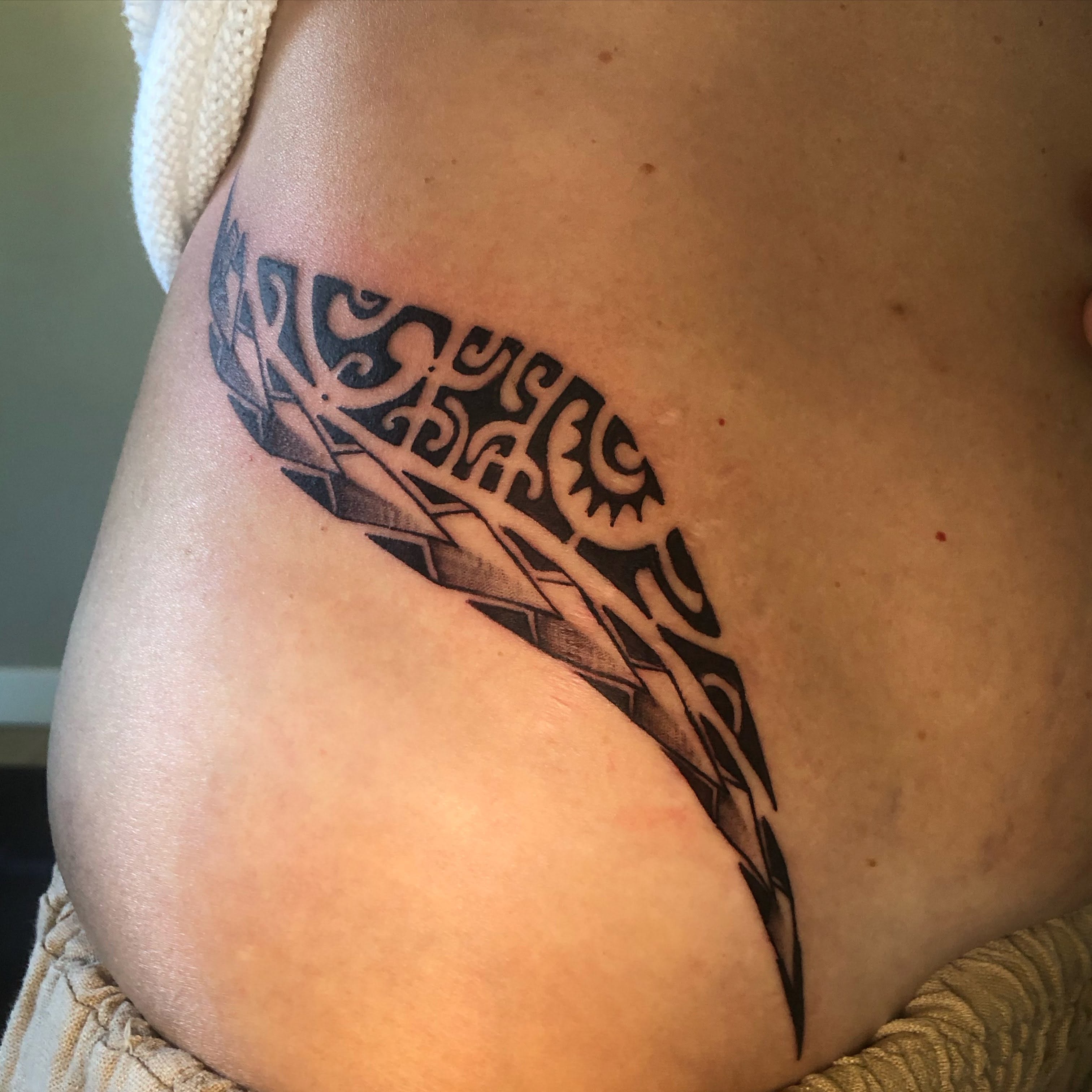 Plume noire aux motifs graphiques tatouée sur le flanc